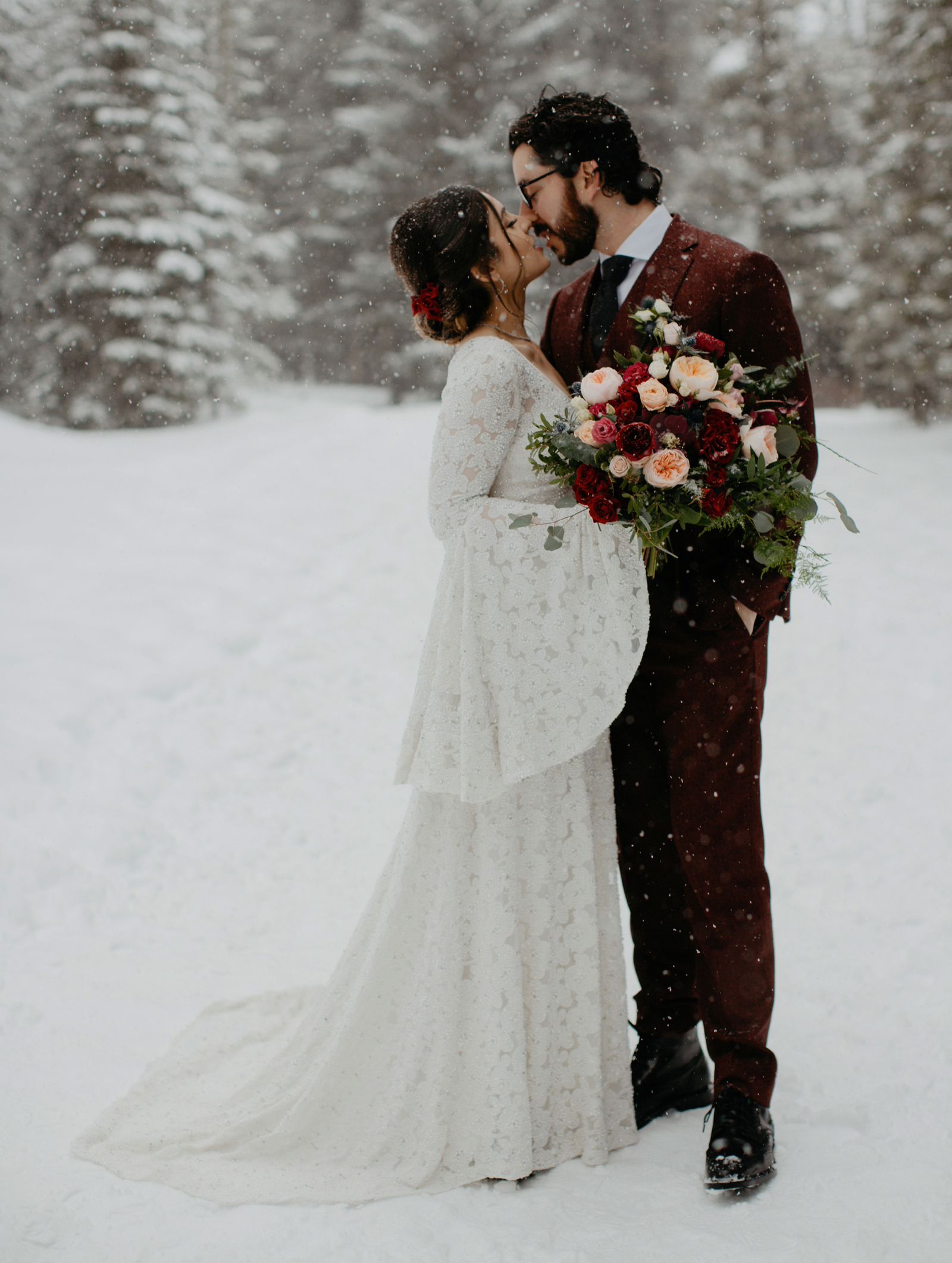 Stylish couple with maroon groom suit and bell sleeved sequence bridal dress in water snowstorm