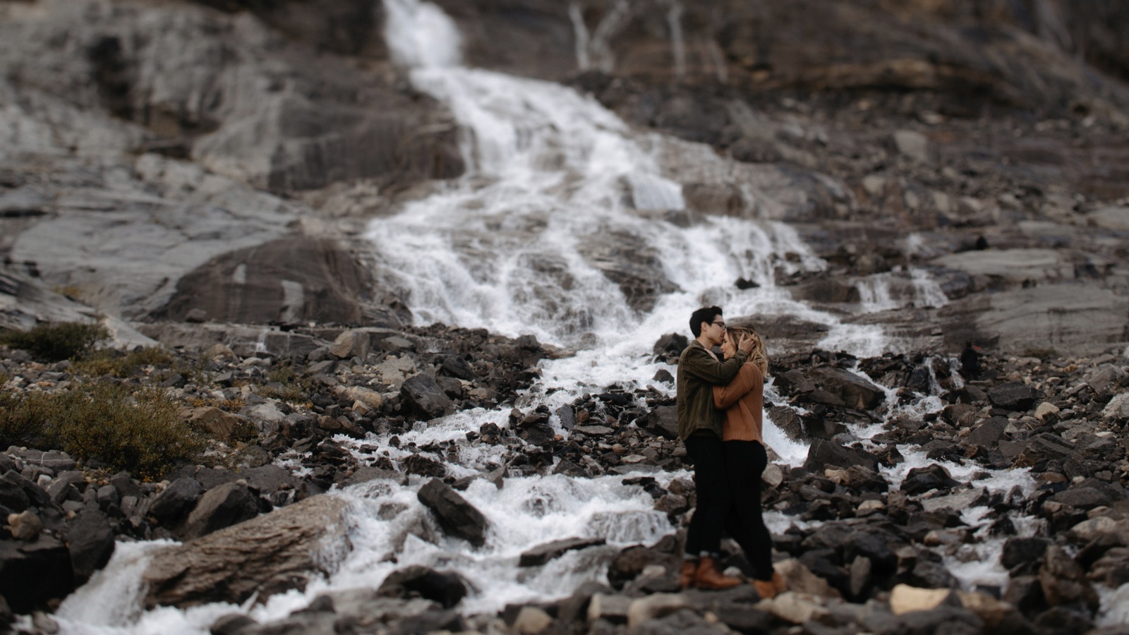 Two people hugging under a secret waterfall in Banff National Park after a short hike