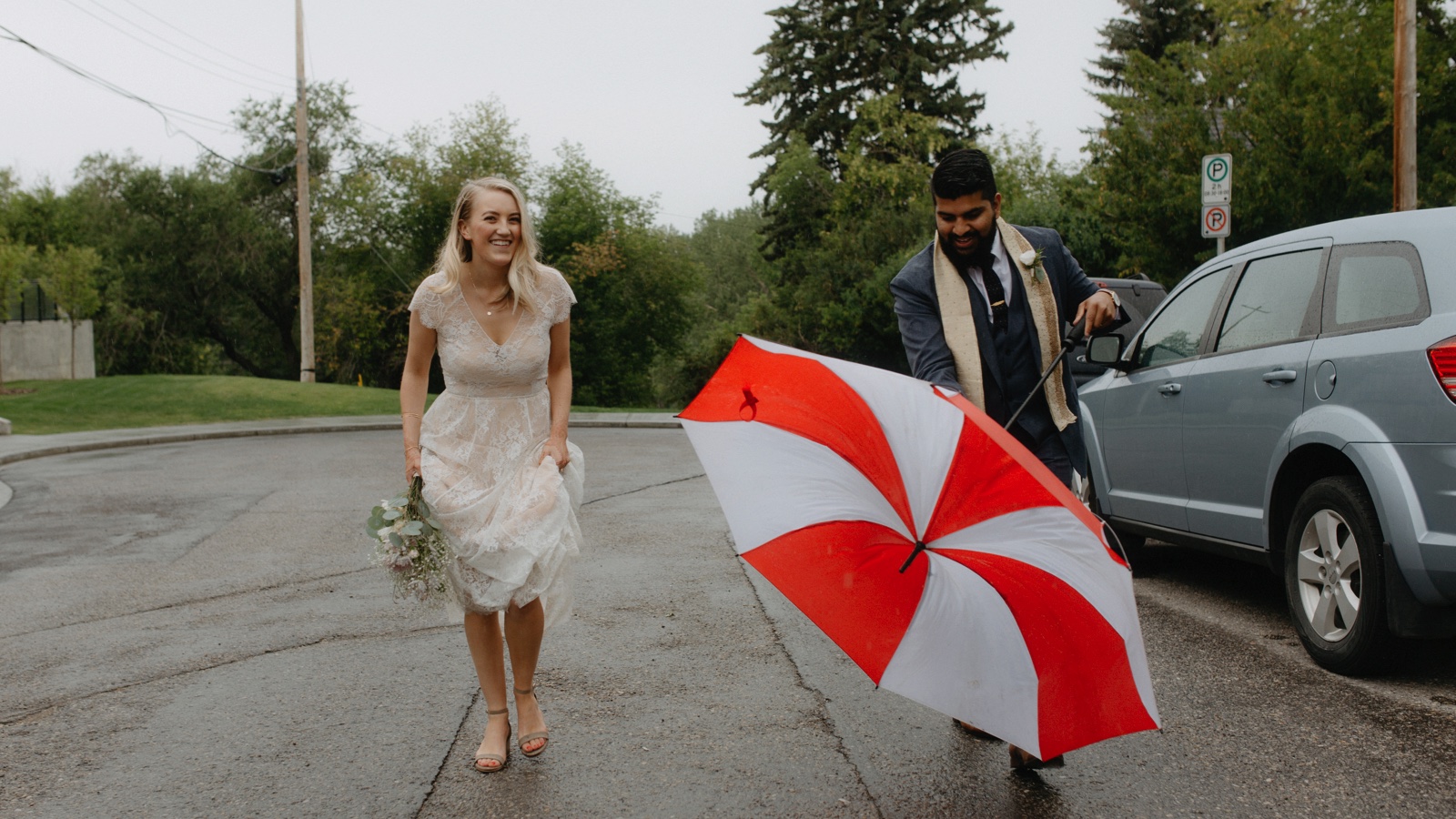 Bride and groom laughing as their umbrella turns inside out on a rainy day