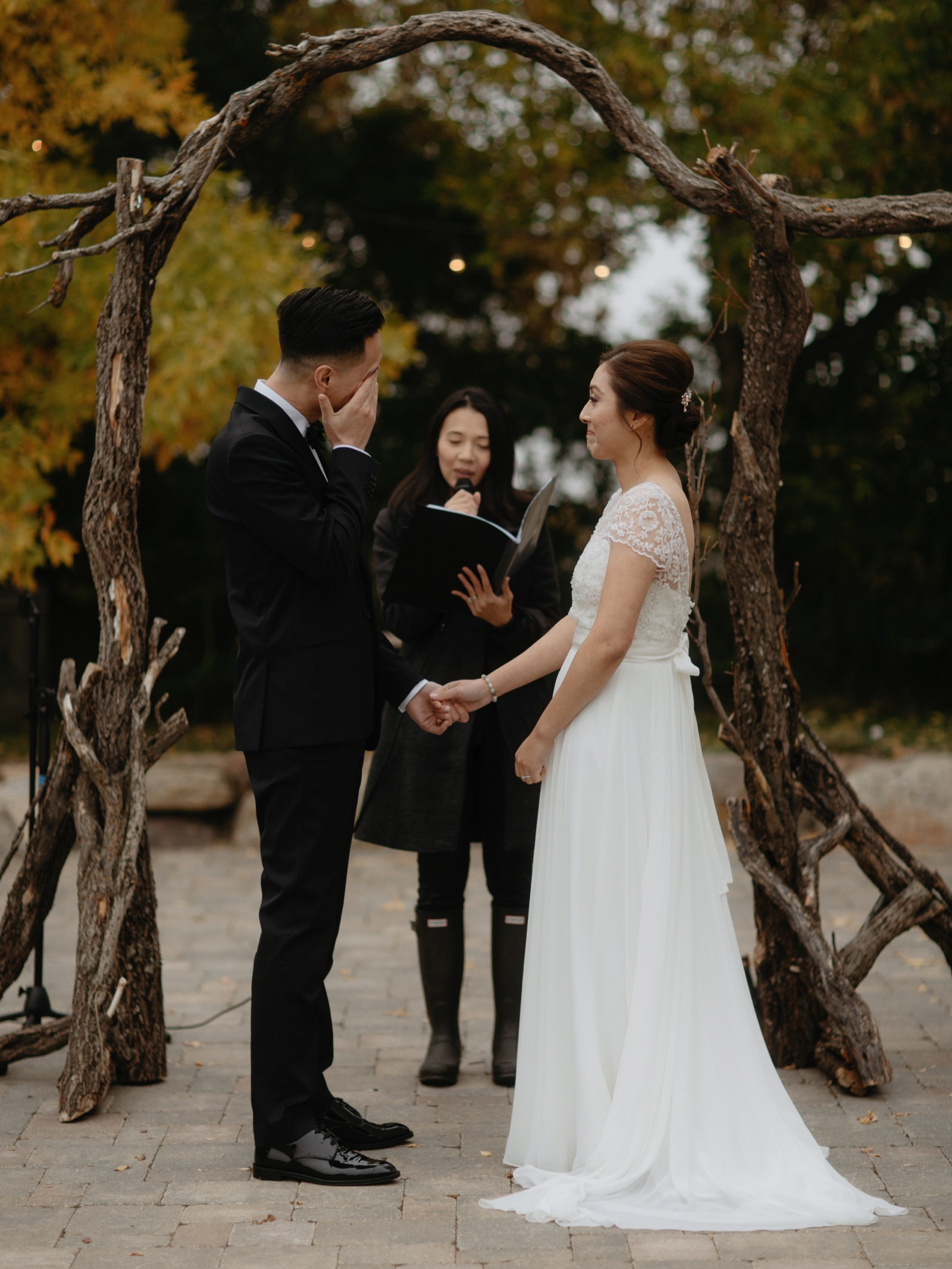 Groom wiping a tear from his eye under a twisted wood arch