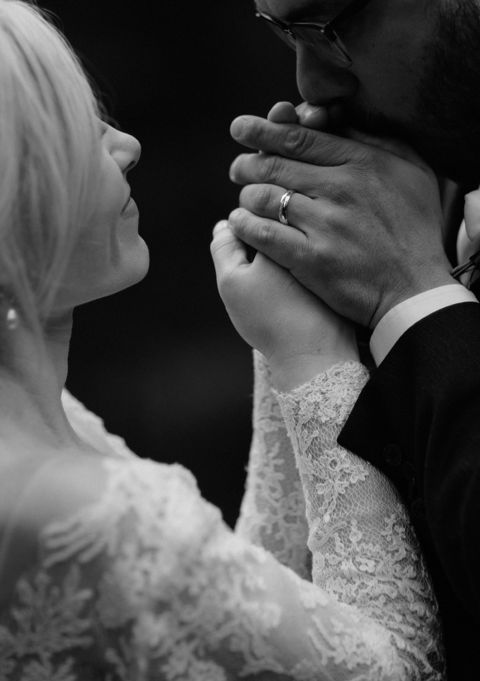 Black and white intimate wedding photography as groom keeps his bride's hands warm by blowing on them