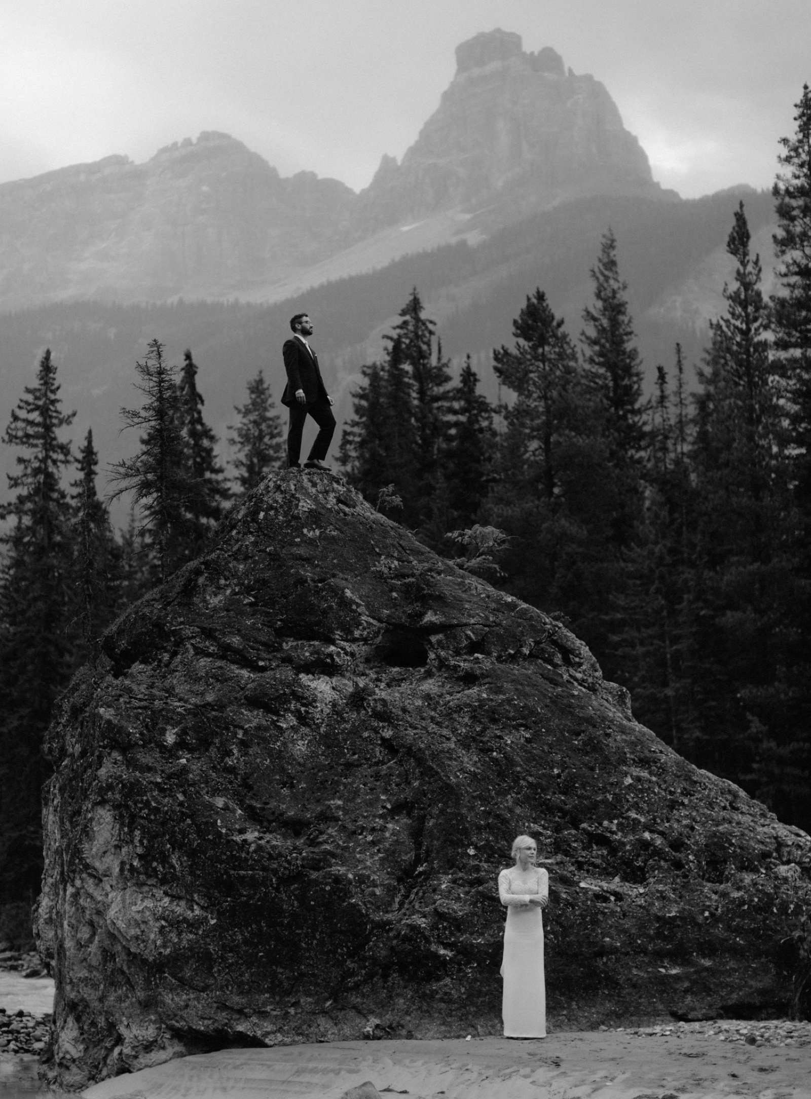 Groom climbing on a large boulder with a mountainous backdrop