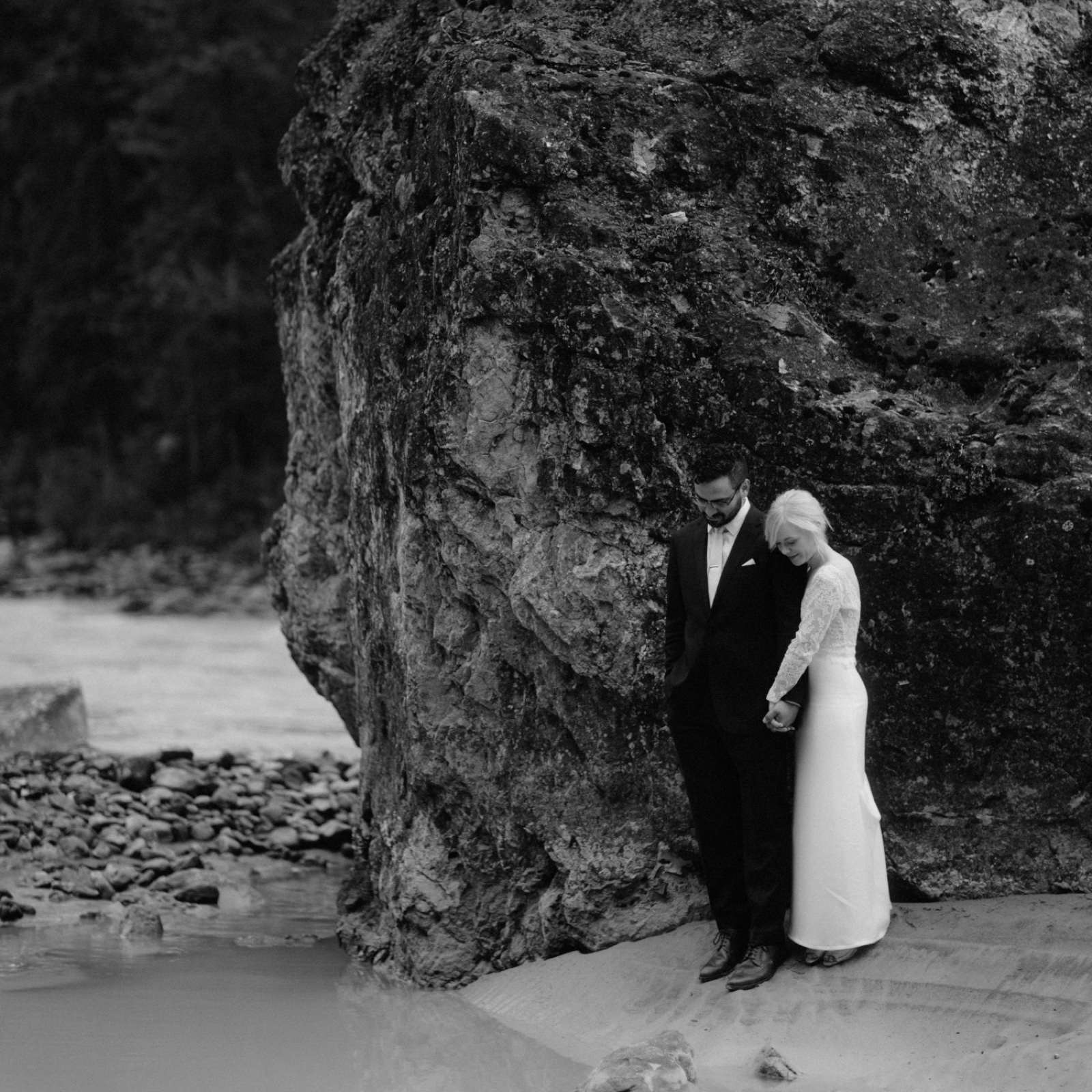 Couple standing together beside a large mountain boulder at a hidden location in Yoho