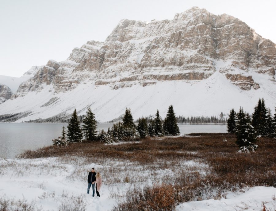Couple in a meadow with fresh snow and a mountainous backdrop at their anniversary photography session at Bow Lake