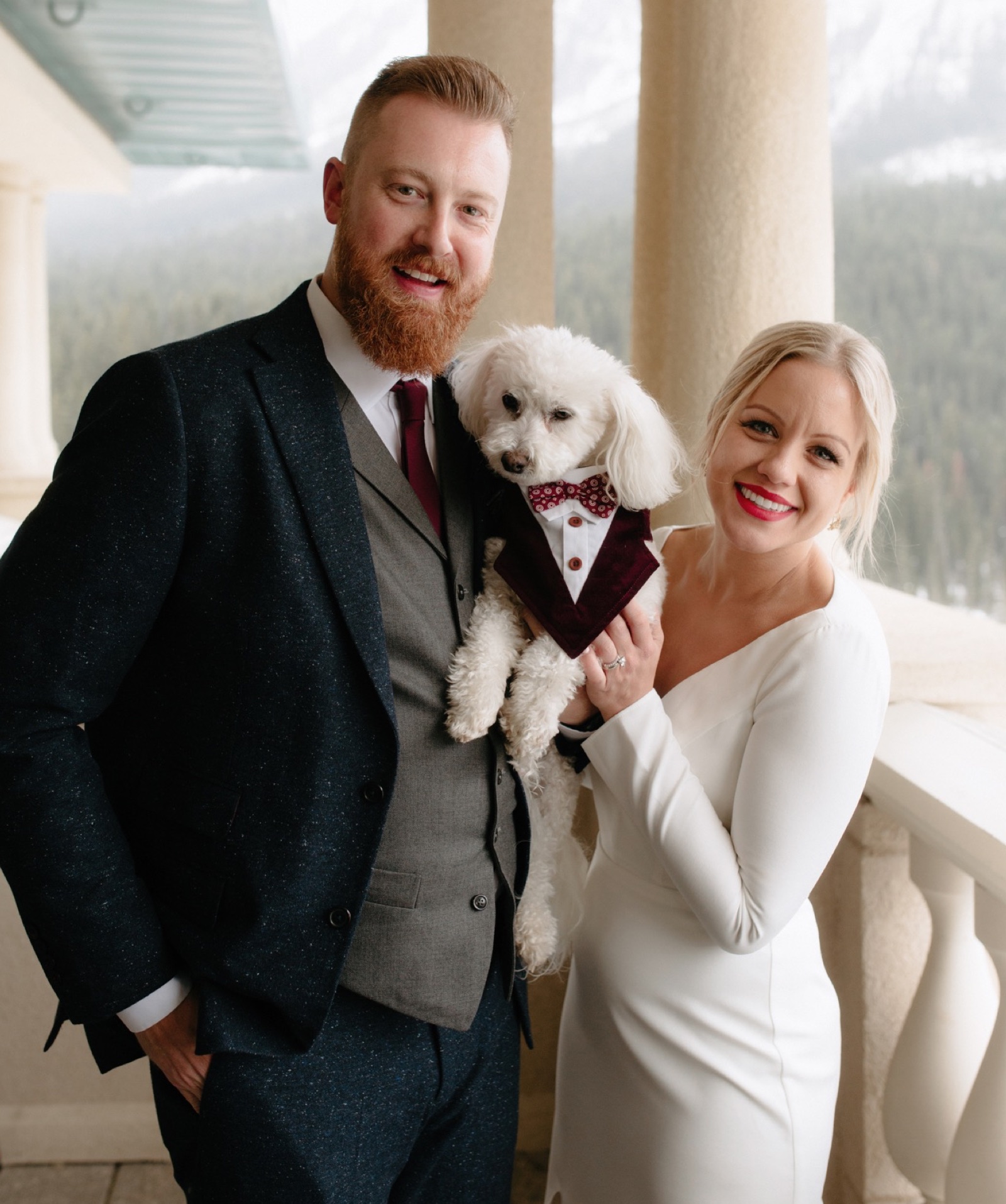 Winter wedding couple on their patio overlooking Lake Louise with their dog Zeus in a tuxedo