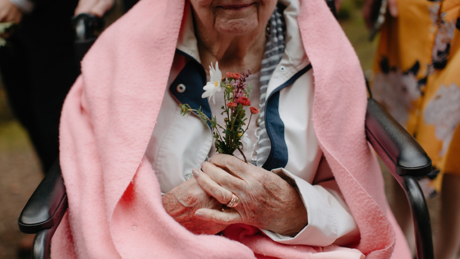 Grandma wrapped in a pink blanket holding onto florals handed to each guest prior to the wedding ceremony
