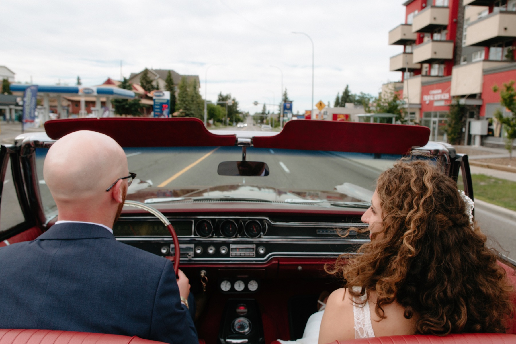 Wedding couple driving the streets of Calgary in their red vintage getaway vehicle