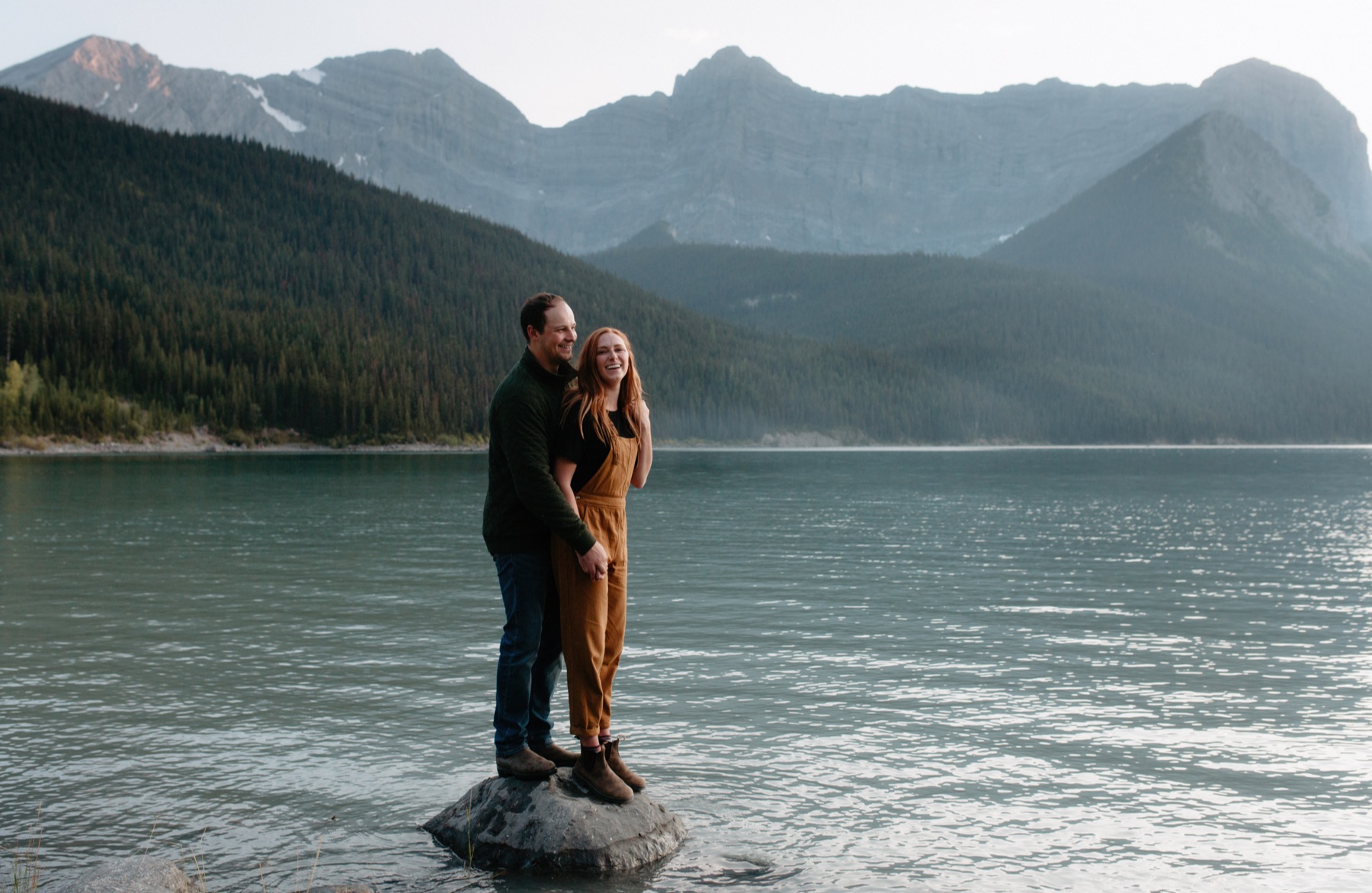 Casual engagement session in Kananaskis, South of canmore, as couple stands laughing on a rock