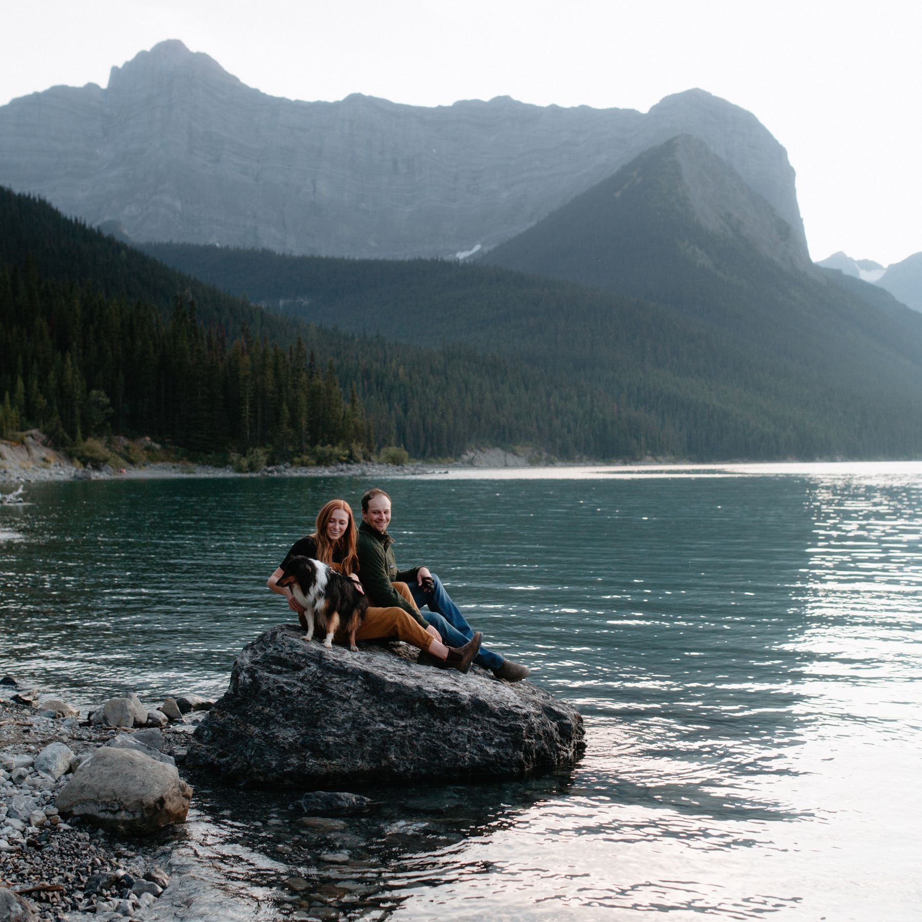Intimate couple session at Upper Kananaskis Lake with couple sitting on a half submerged boulder looking towards Sarrail Ridge