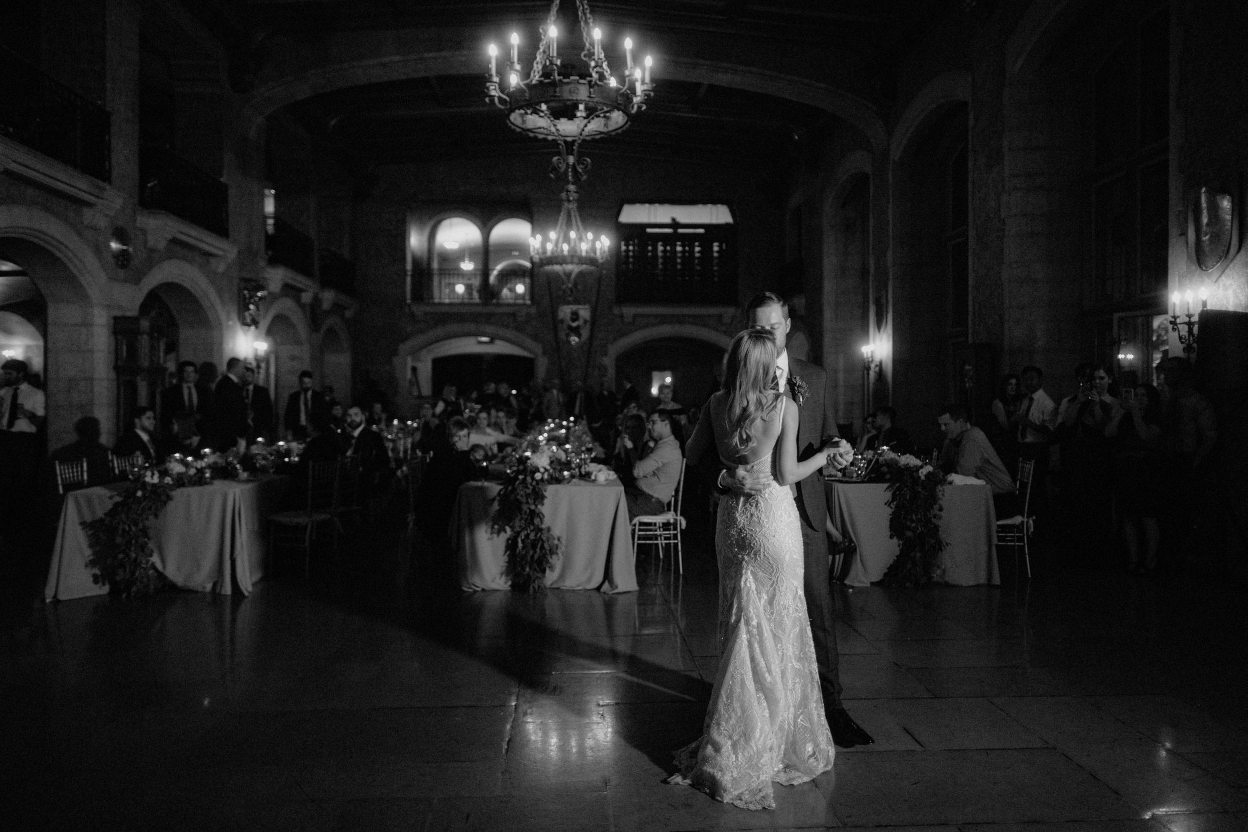 Traditional first dance with couple swaying under chandeliers as their guests look on from their tables