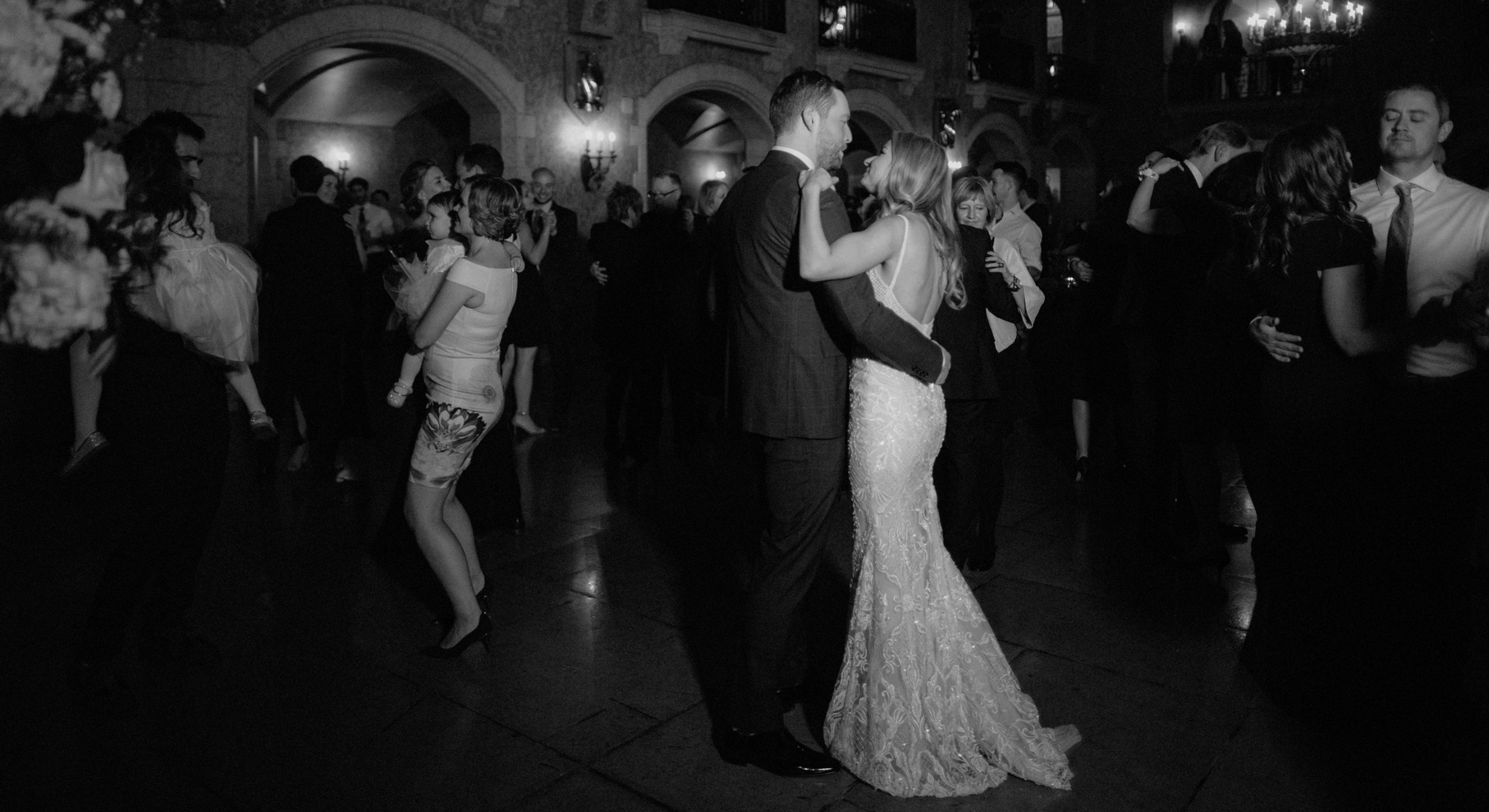 Bride and groom dancing amongst their guests in a chandelier lit stone hall