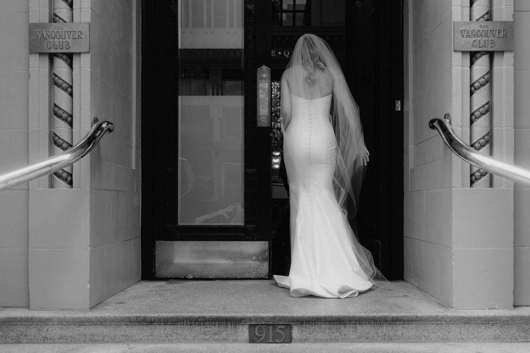 Bride wearing A-line dress and cathedral length veil entering The Vancouver Club front doors