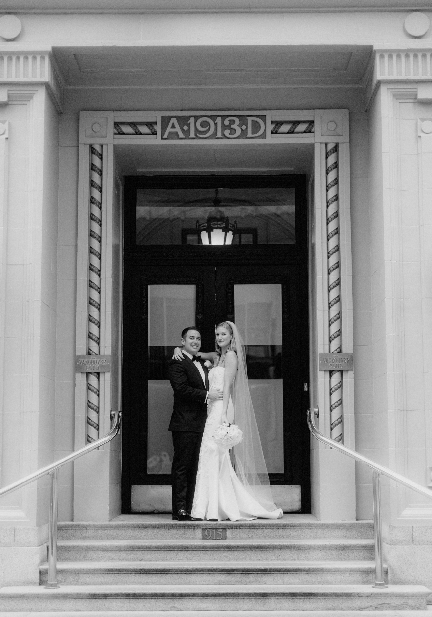 Timless black tie wedding potraits on historic stone steps infront of The Vancouver Club with A1913D inscribed above them