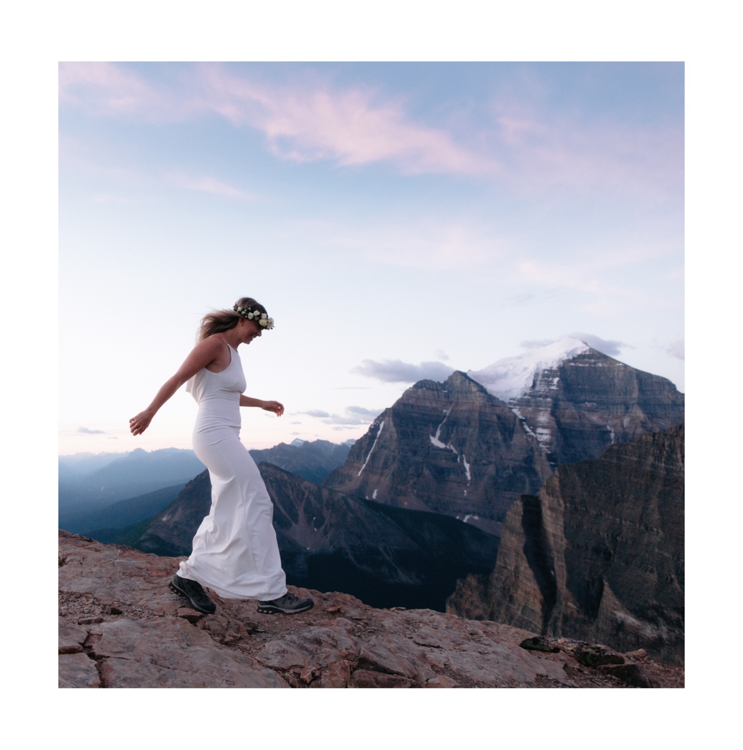Bride wearing a form fitting white bridal dress and hiking boots skipping to her first look with Mount Temple in the background