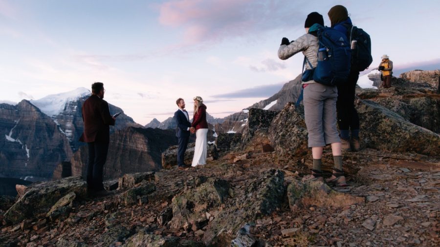Intimate sunrise elopement in Banff National Park with three friends looking on as alpenglow reflects off the Canadian Rockies
