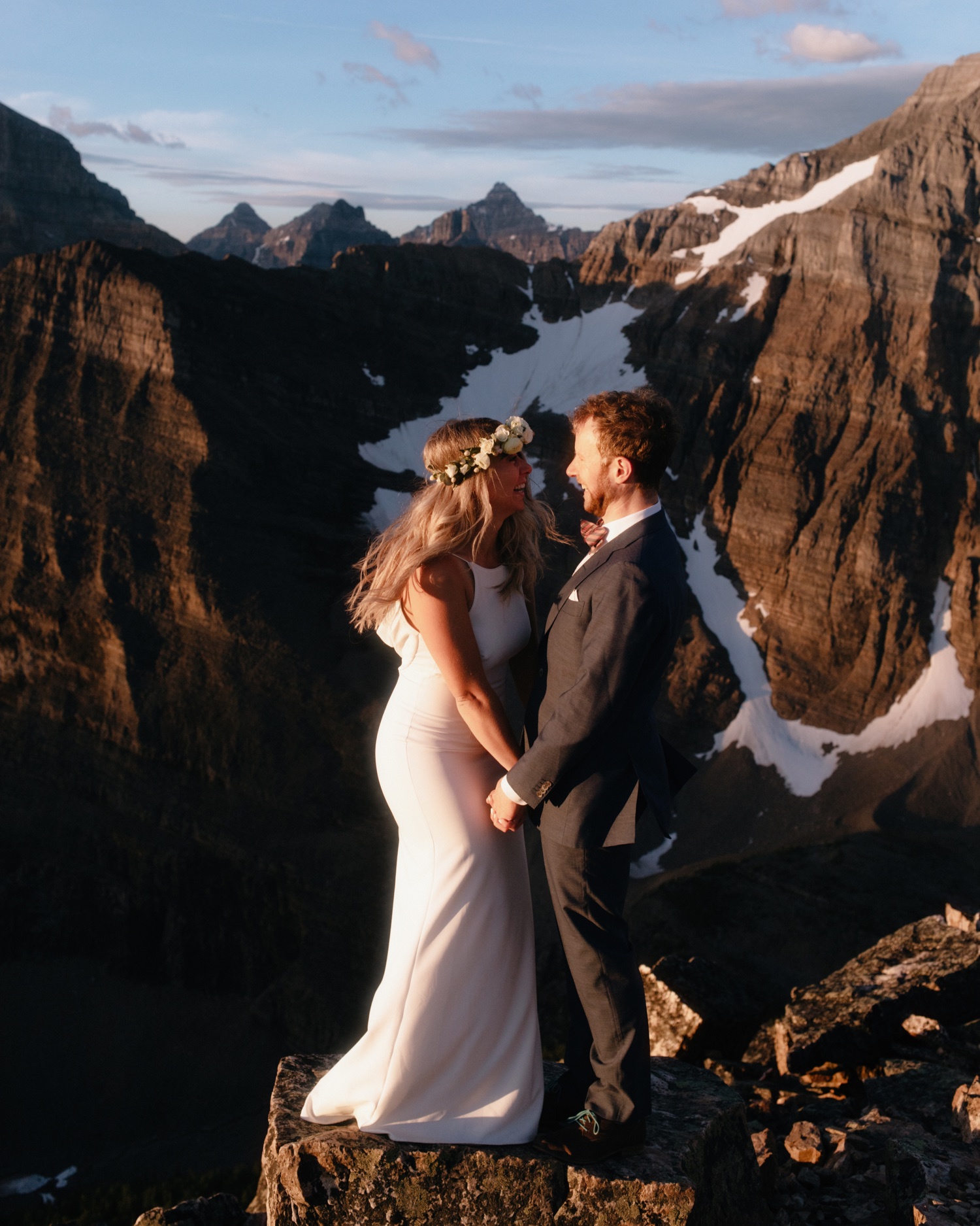Couple awash in morning sunlight holding hands facing each other with Mount Aberdeen of the Canadian Rockies behind them