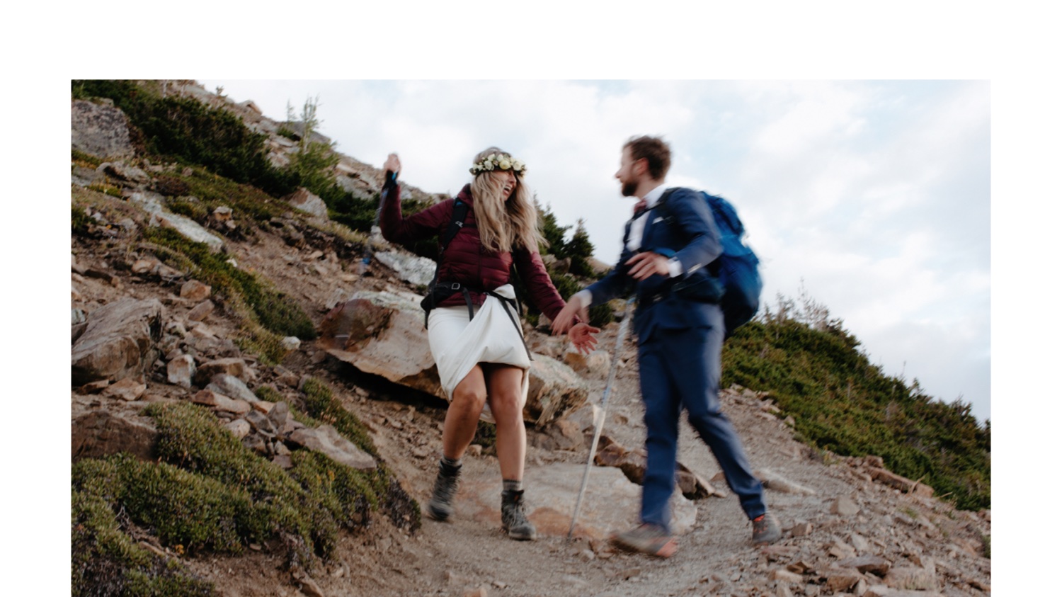 Eloped man and woman holding hands as they hike down a steep mountain after a sunrise elopement ceremony