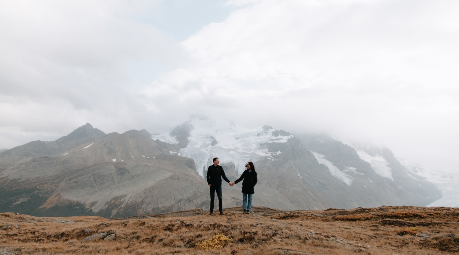 Ridge engagement photography session up the Icefields Parkway with couple holding one hand looking at each other