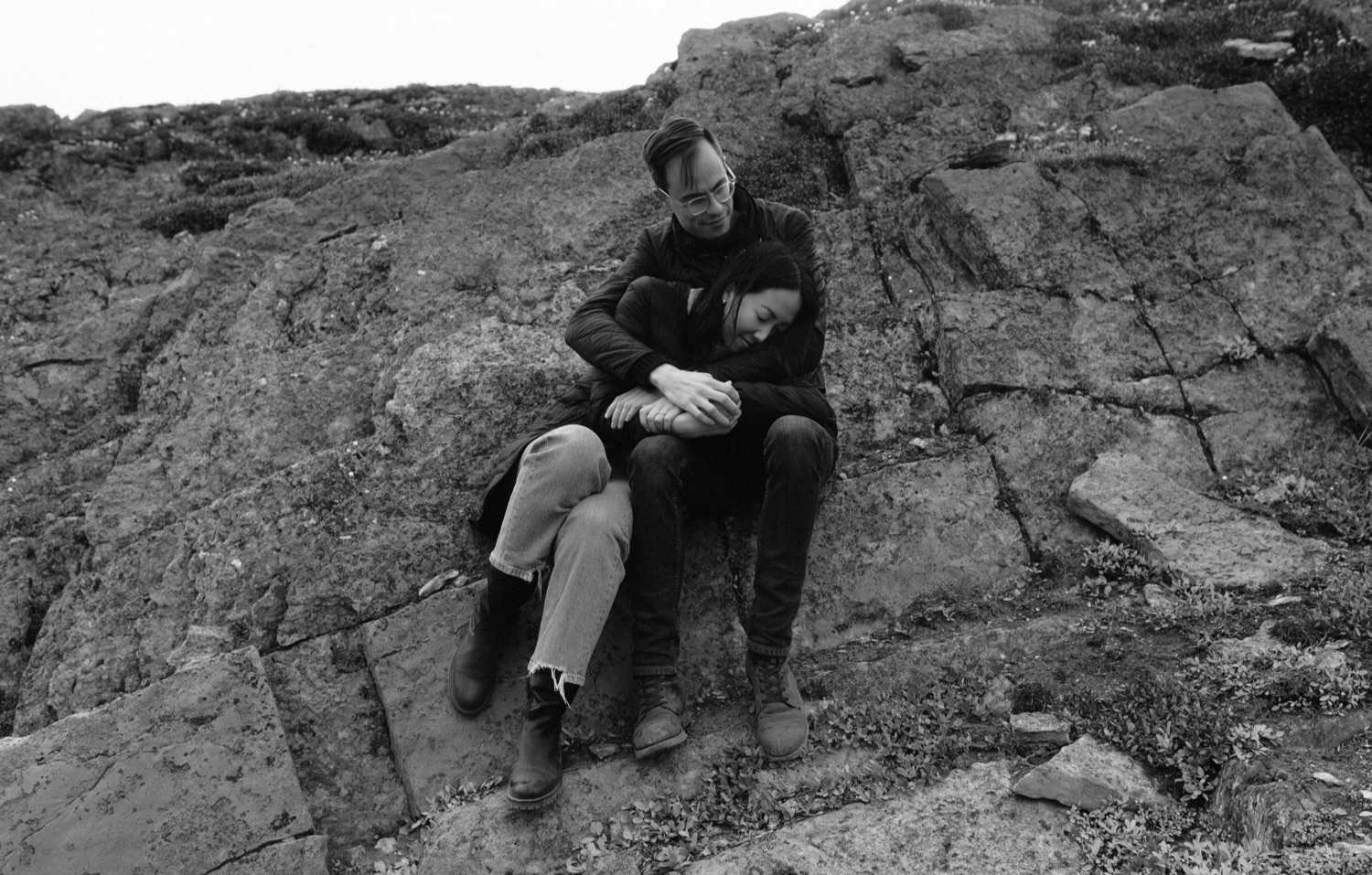 Couple embracing while sitting on a rock ridge for a hiking engagement session