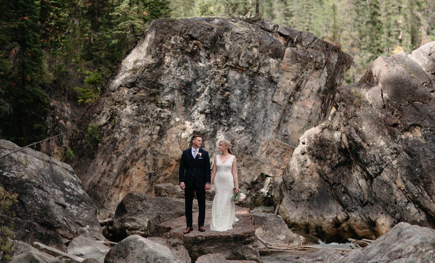 Newly eloped couple posing near Cathedral Mountain Lodge near a toppled boulder