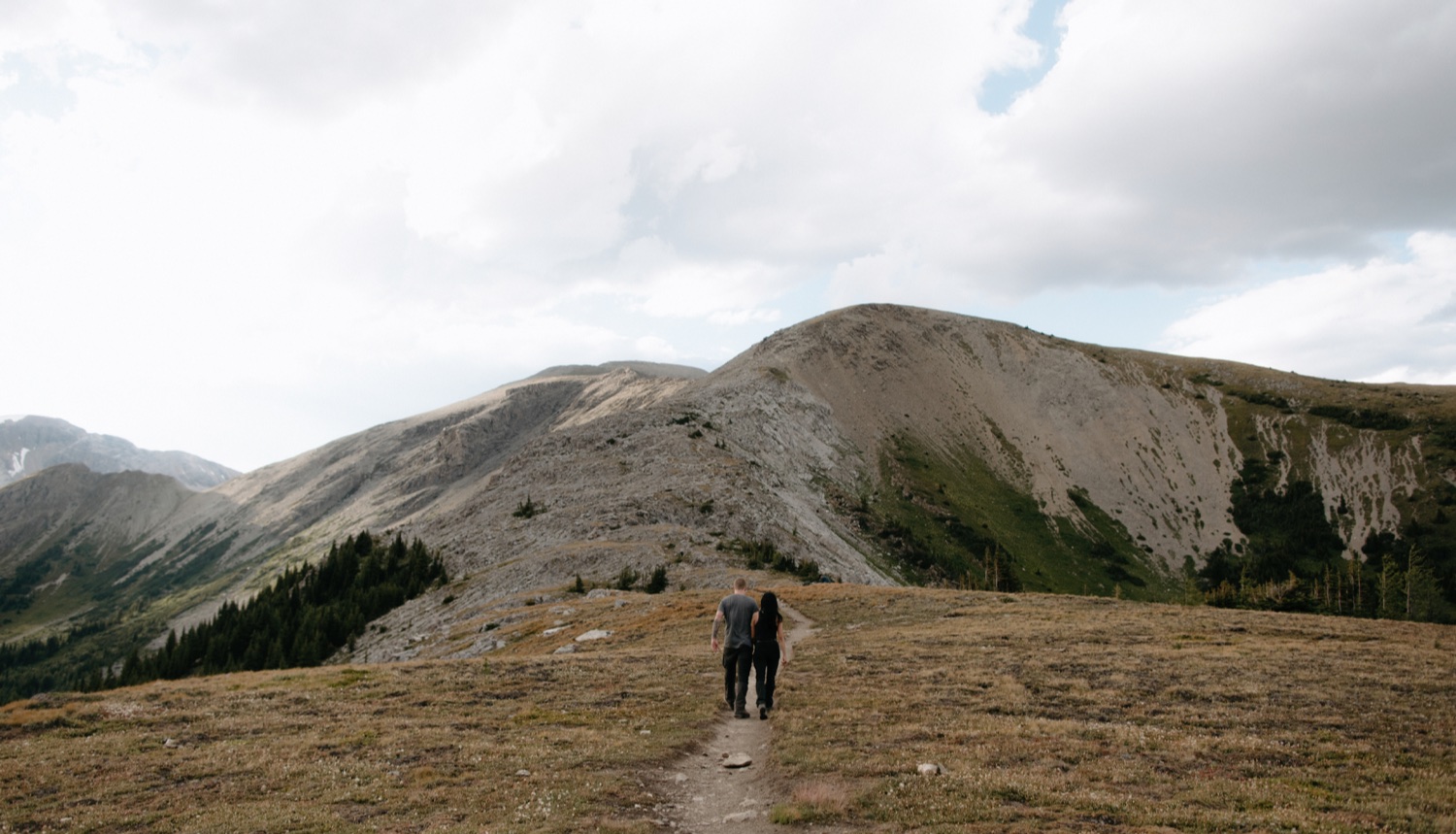 Couple hiking wearing dark gear hand in hand towards the Nublet and Nub Peak on an autumn day