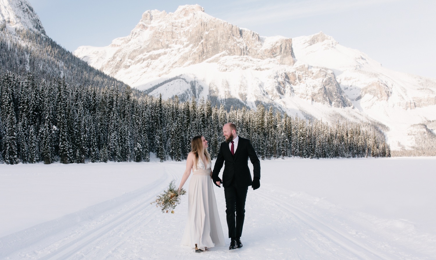 Bride wearing mauve truvelle bridal dress and dried floral bouquet on frozen Emerald Lake in Yoho National Park