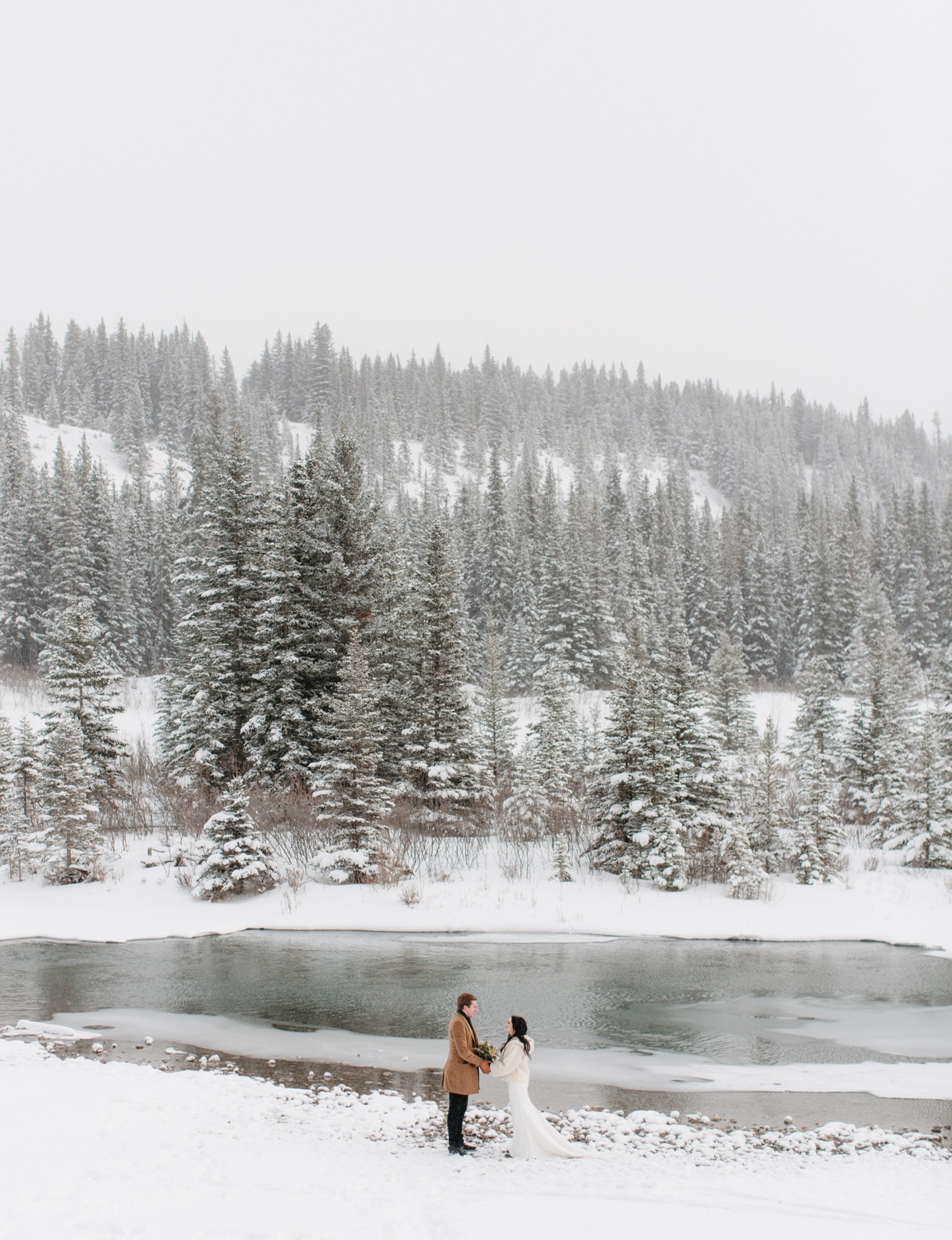Newly married couple winter wedding portraits in Banff near open water