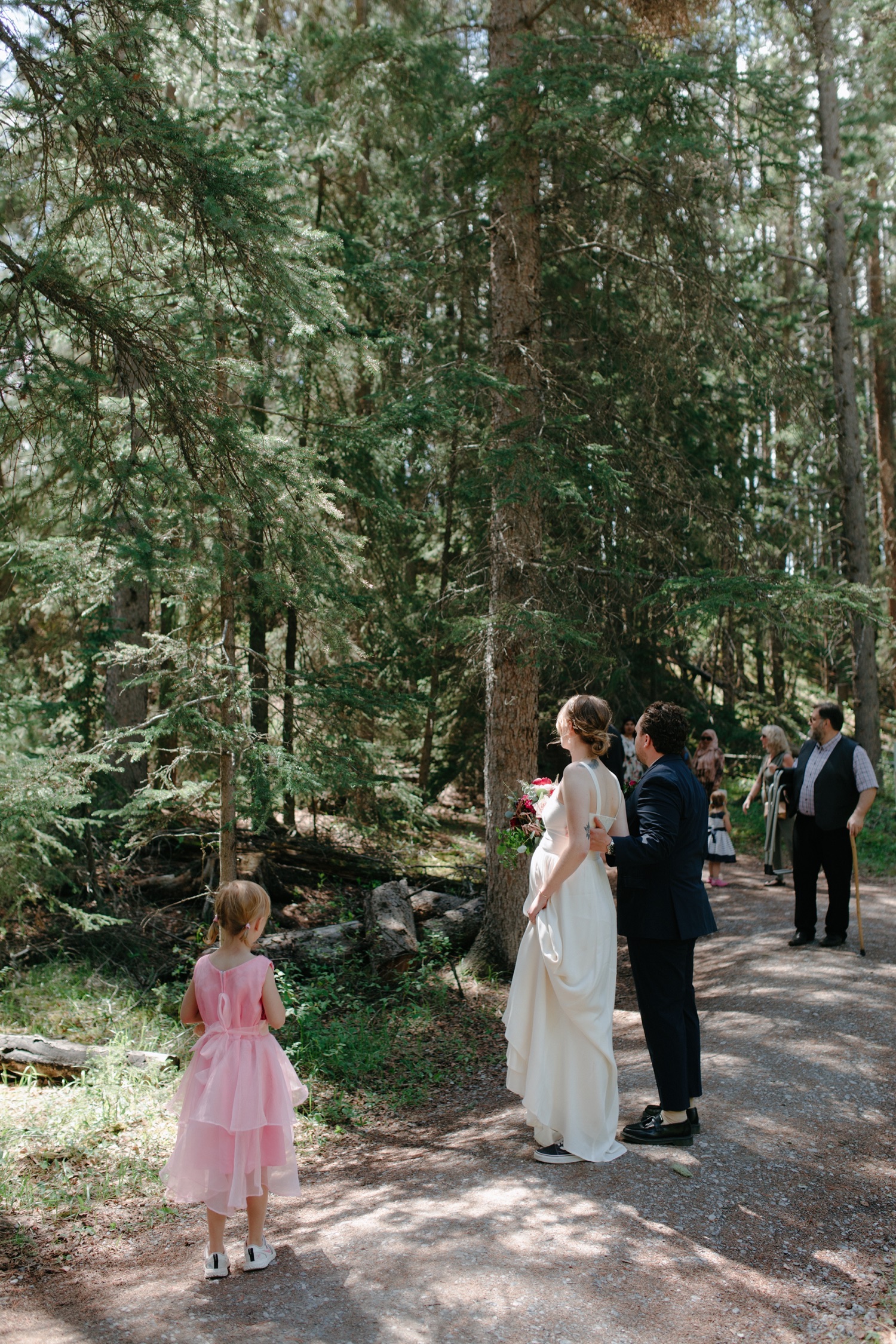 Couple embracing as they look back on a dappled lit forest path making sure their guests are managing the hike