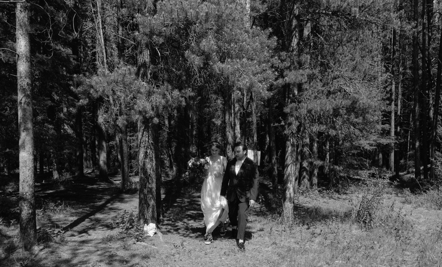 Wedding couple walking themselves down the aisle to their wedding ceremony, exiting a dappled forest