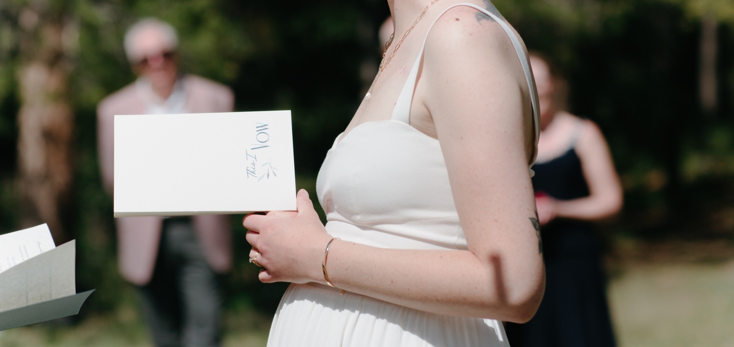 Bride holding That I Vow booklet with a slight baby bump