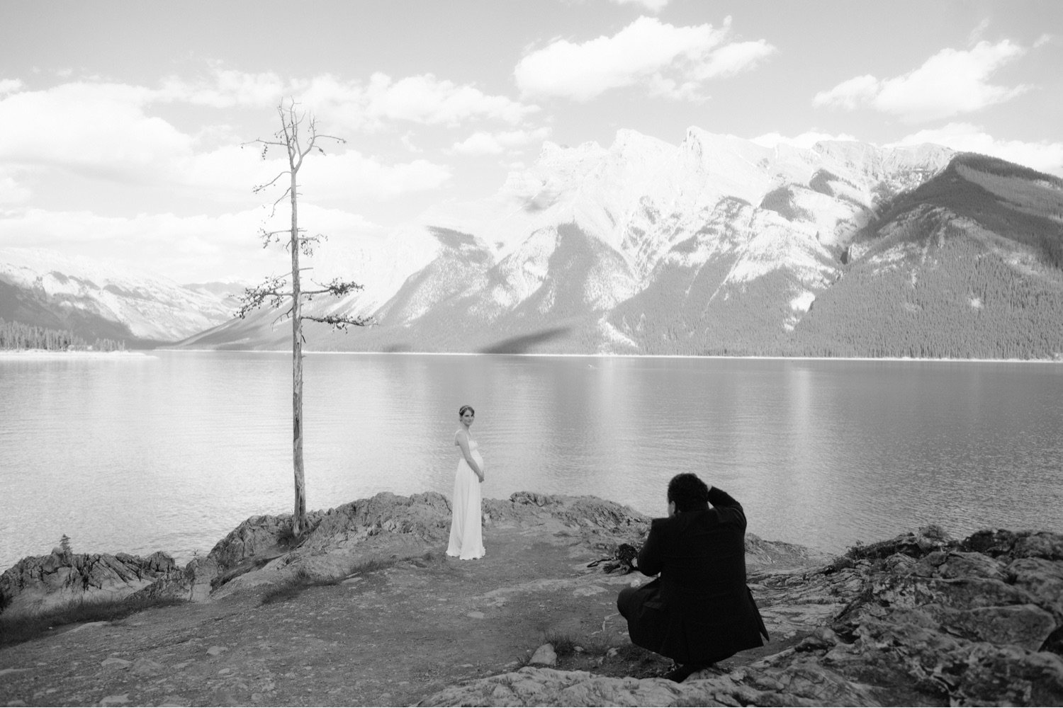 Groom taking film photo of his expecting bride at Lake Minnewanka