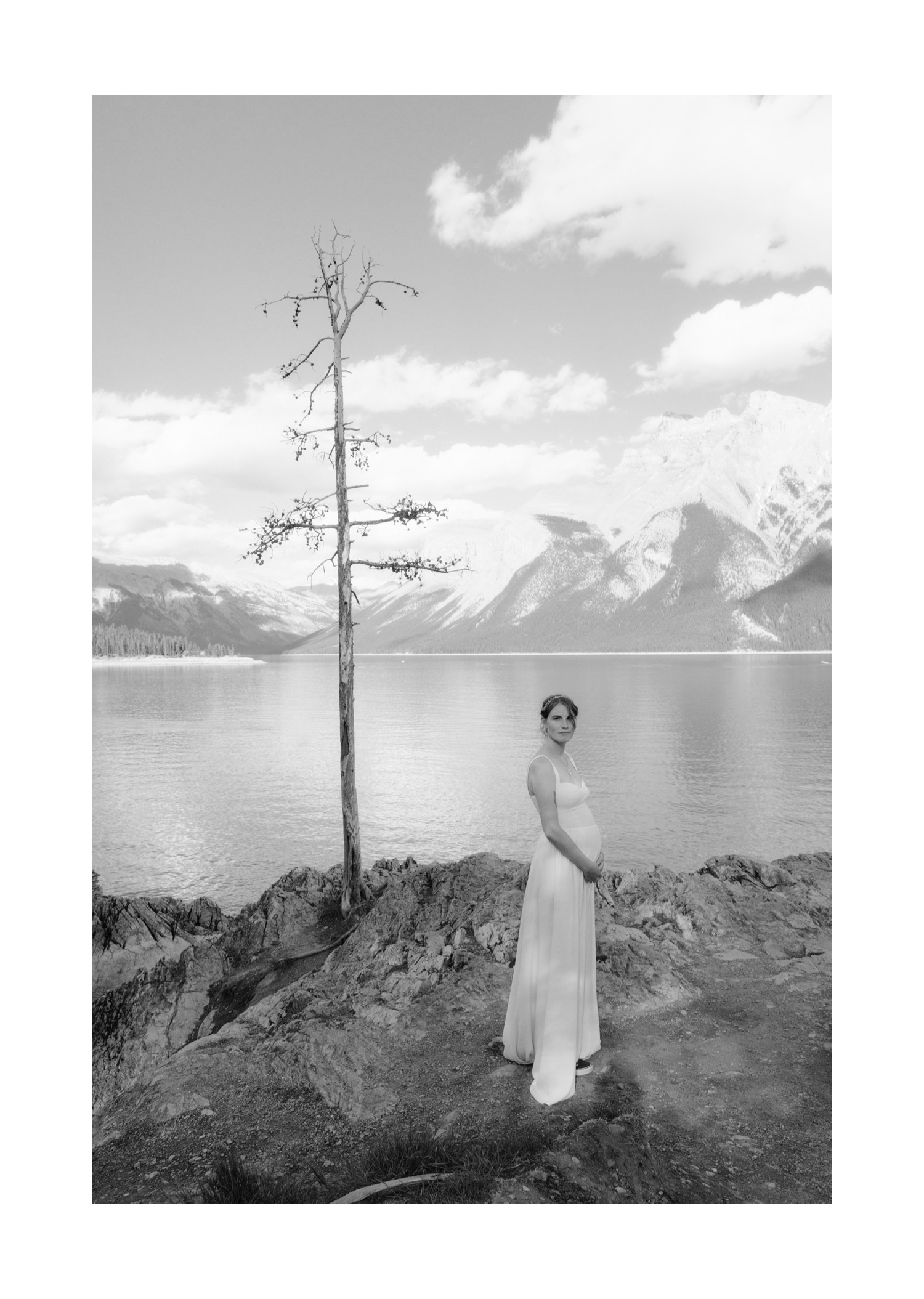 Pregnant bride black and white wedding portrait on the shores of Lake Minnewanka with a lone dead tree mirroring her