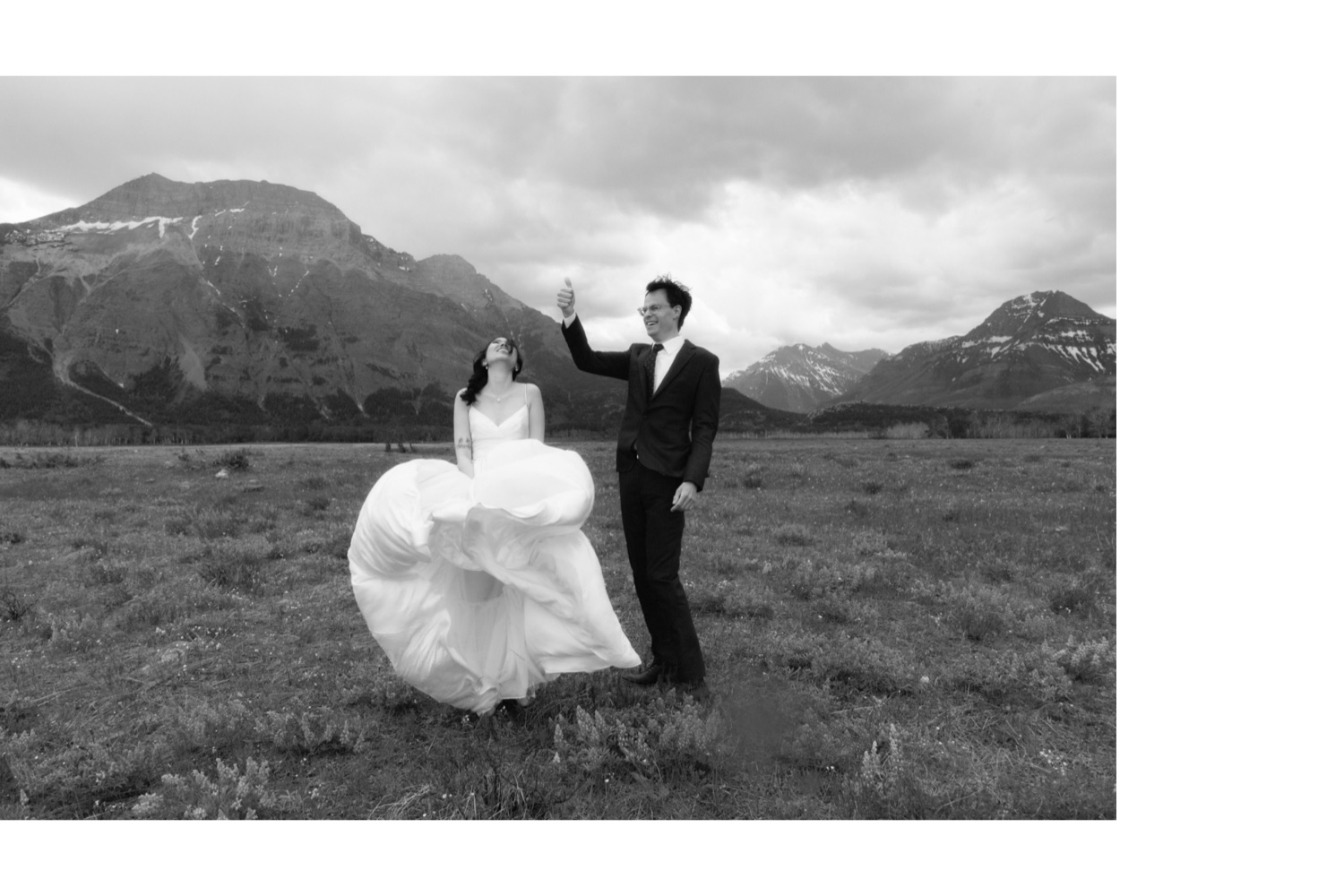 Groom giving the thumbs up as the bride's dress of blown all about by the wind in Waterton