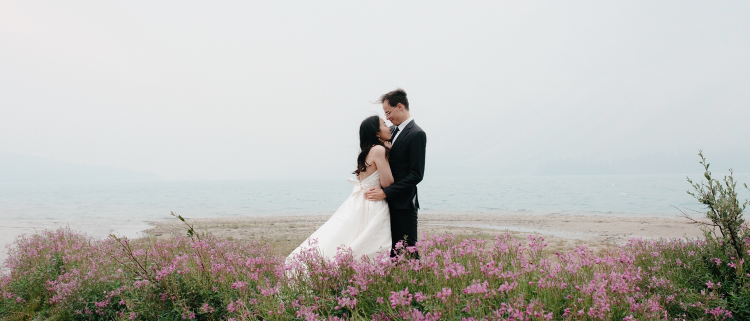 Newly married couple embracing in bridal attire amongst the fireweed at Bow Lake