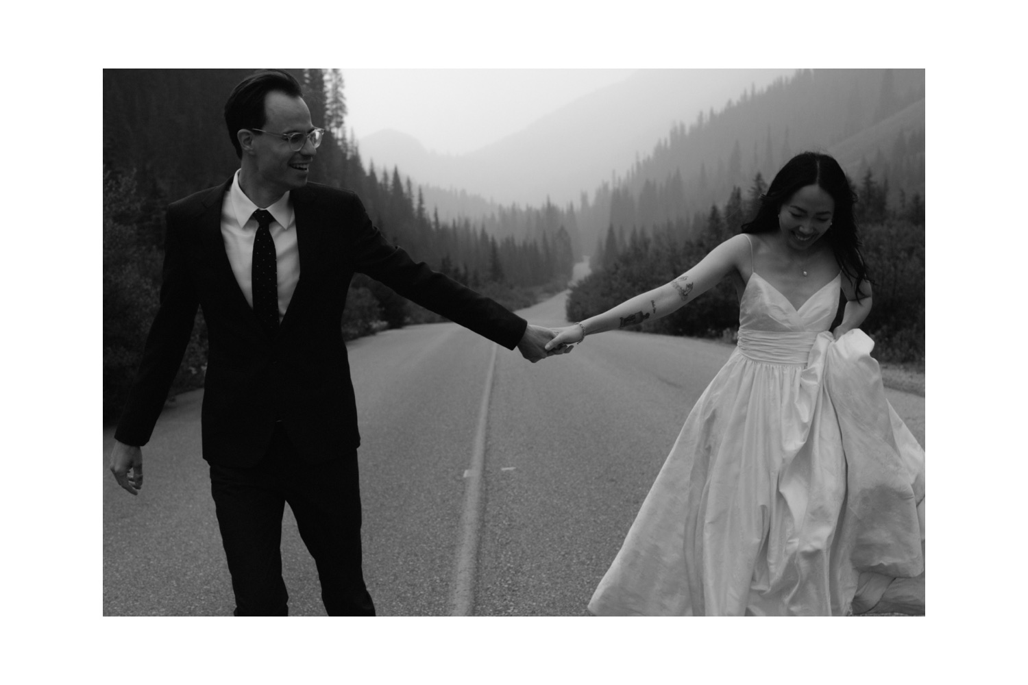 Moody mountain wedding portraiture in Canada with couple running hand in hand down the road