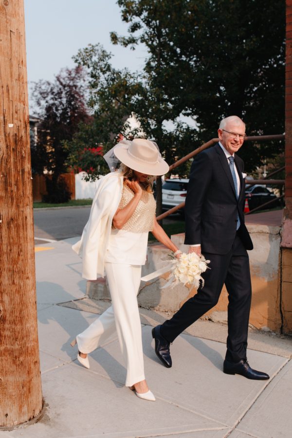 Eloped couple with impeccable style of tapue hat with tulle, white pantsuit with gold details in Inglewood